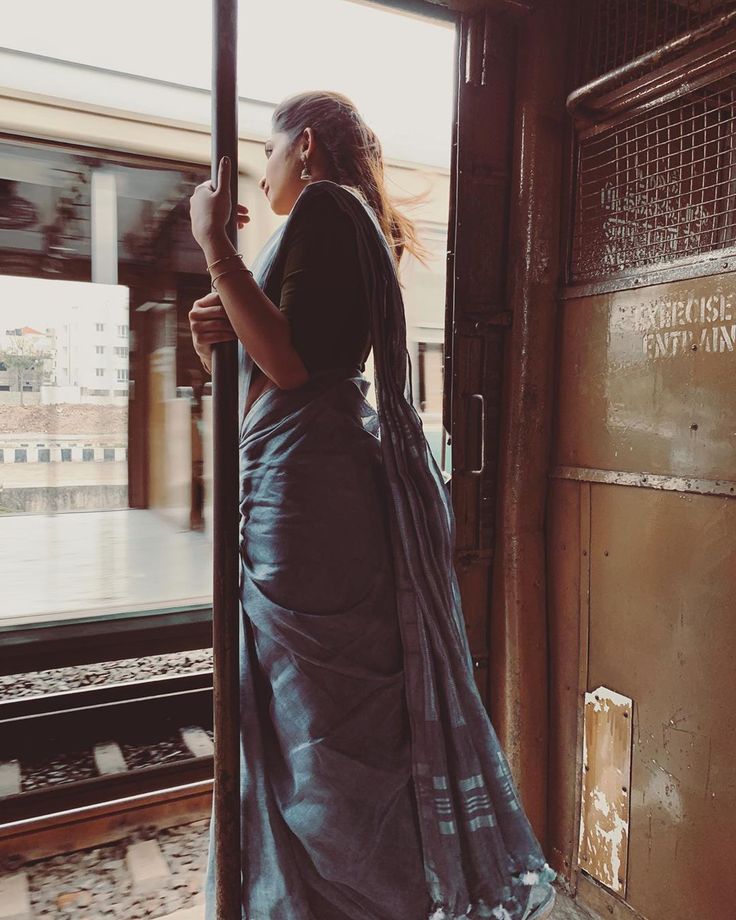 a woman in a long blue dress is standing on the train platform and looking out the window