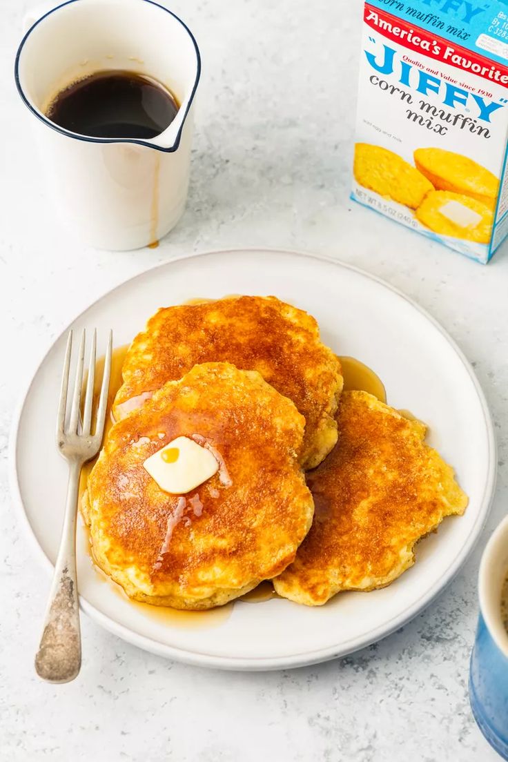 two pancakes on a white plate with butter and syrup next to a cup of coffee