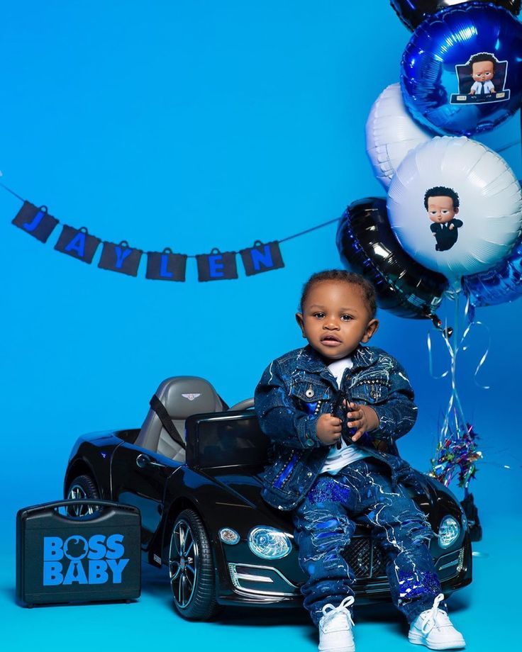 a little boy sitting on top of a toy car with balloons in the shape of boss baby