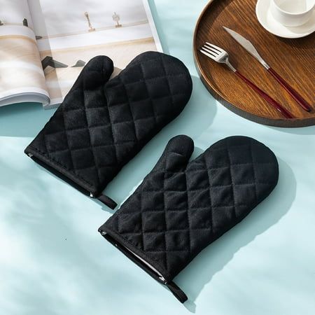 two black oven mitts sitting on top of a table next to a plate and cup