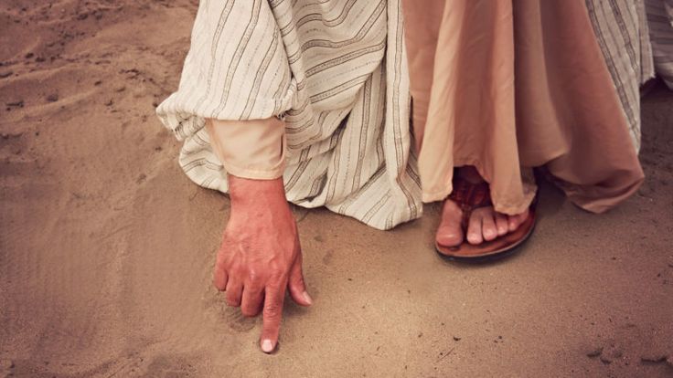 two people standing in the sand with their hands on each other's feet,