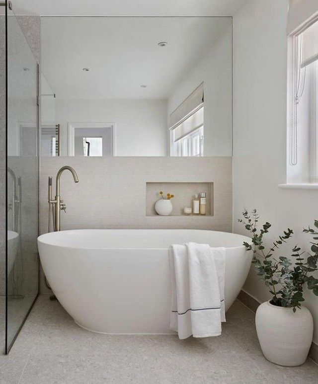 a bathroom with a large white bathtub next to a window and a plant in the corner