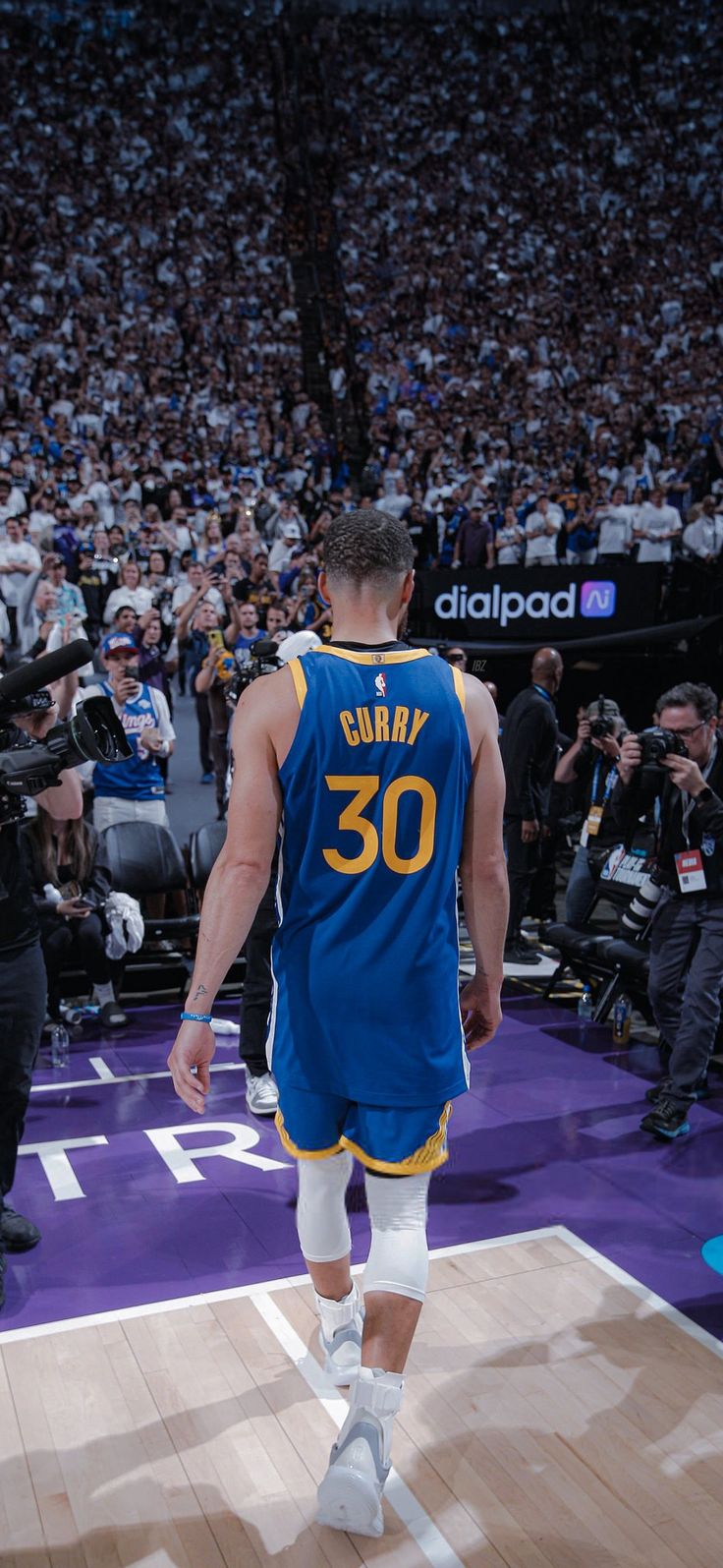 a basketball player walking down the court in front of an arena full of people and photographers