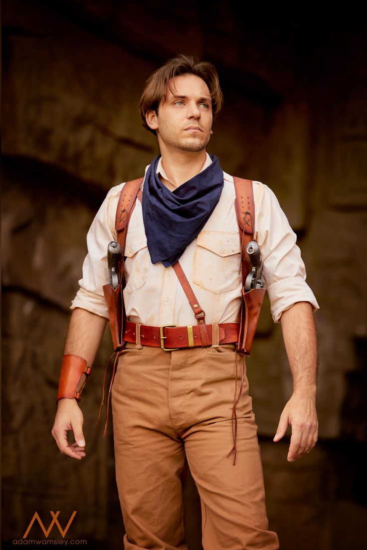 a man with suspenders and a bow tie standing in front of a stone wall