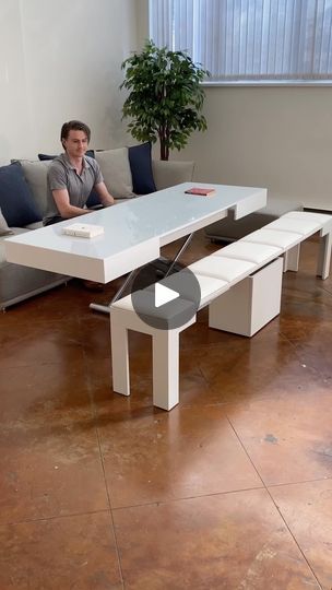 a man sitting on a couch in front of a white table with benches around it