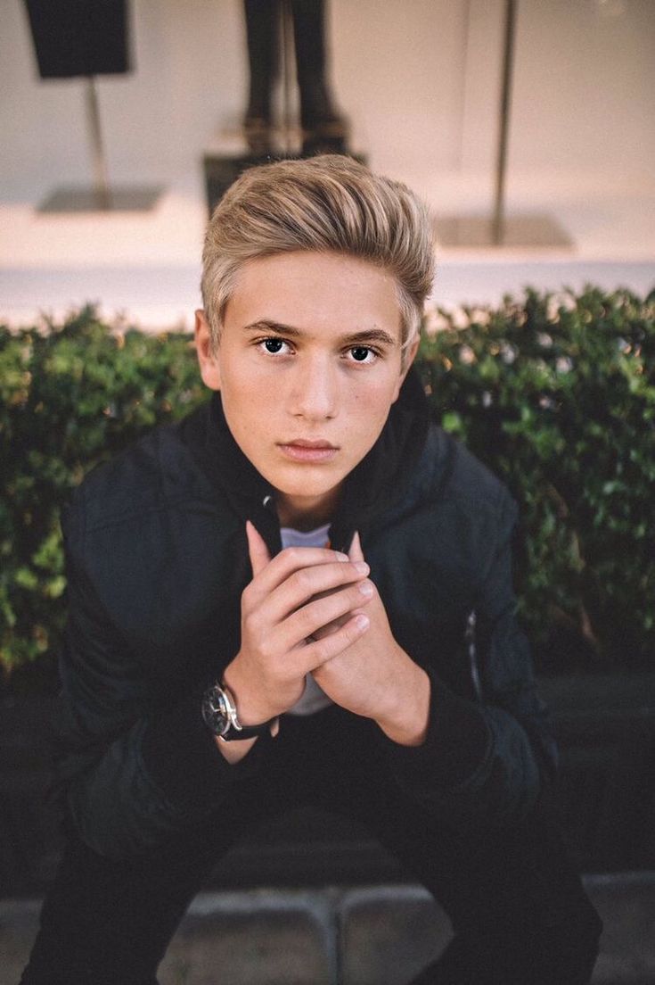 a young man with blond hair and blue eyes is holding his hand up to the camera