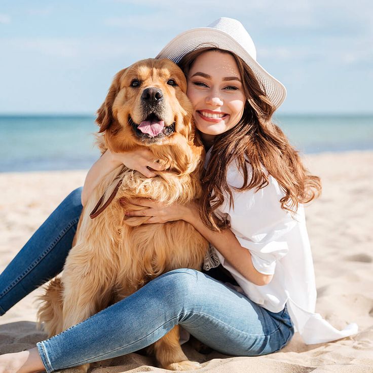 a woman is sitting on the beach with her dog and smiling at the camera,