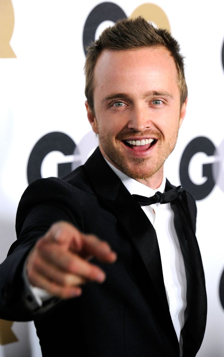 a man in a tuxedo pointing at the camera with his hand out and smiling