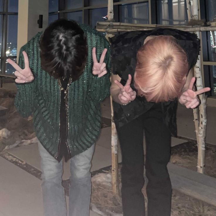 two people standing in front of a window with their hands up and one person making the peace sign