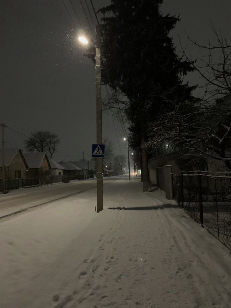 a street light on a pole in the middle of a snow covered road at night