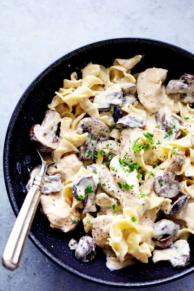 a black bowl filled with pasta and mushrooms on top of a gray table next to a silver spoon