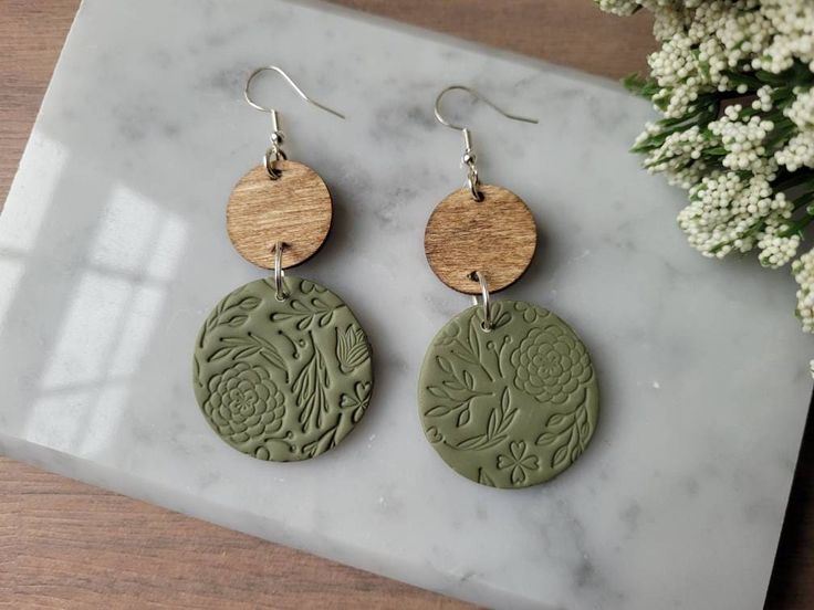 two circular wooden earrings with floral designs on them sitting on a marble slab next to flowers