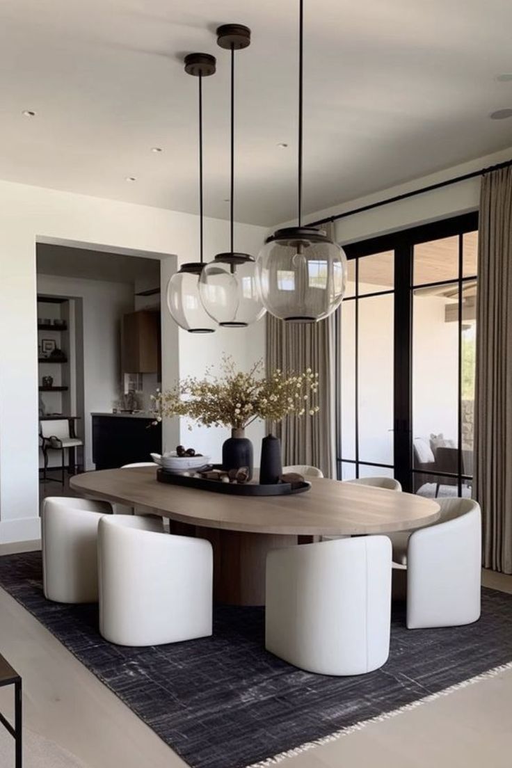 a dining room table with four chairs and a vase on top of it in front of large windows