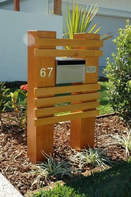 a wooden mailbox sitting in the middle of a flower bed next to a house