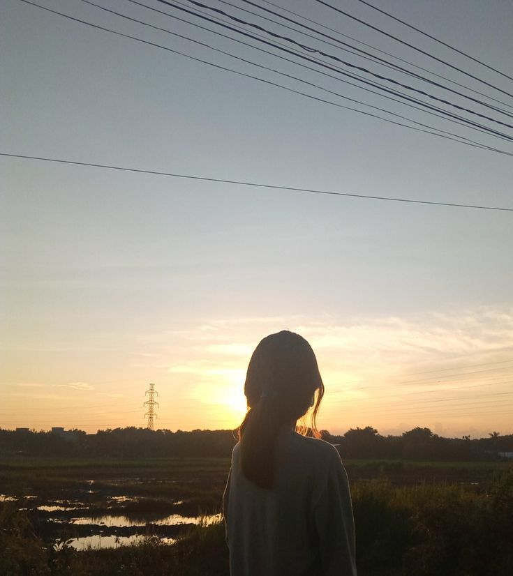 a woman standing in front of the sun with her back turned to the camera,