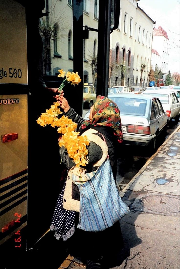 a woman is standing on the sidewalk with flowers in her hand