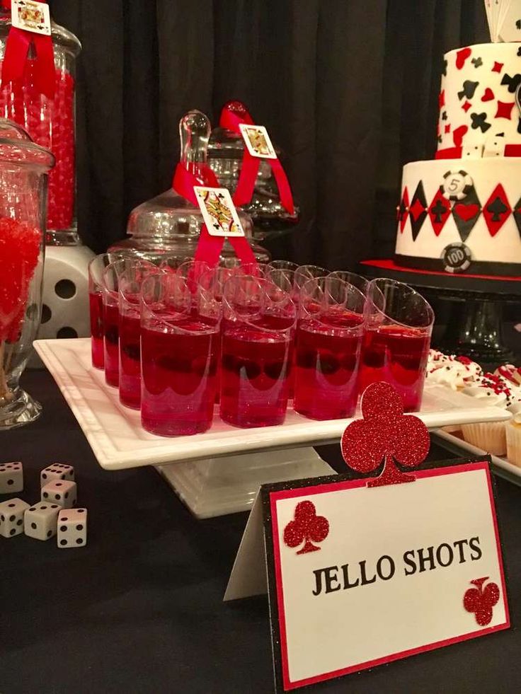 a table topped with lots of glasses filled with red liquid next to cakes and desserts