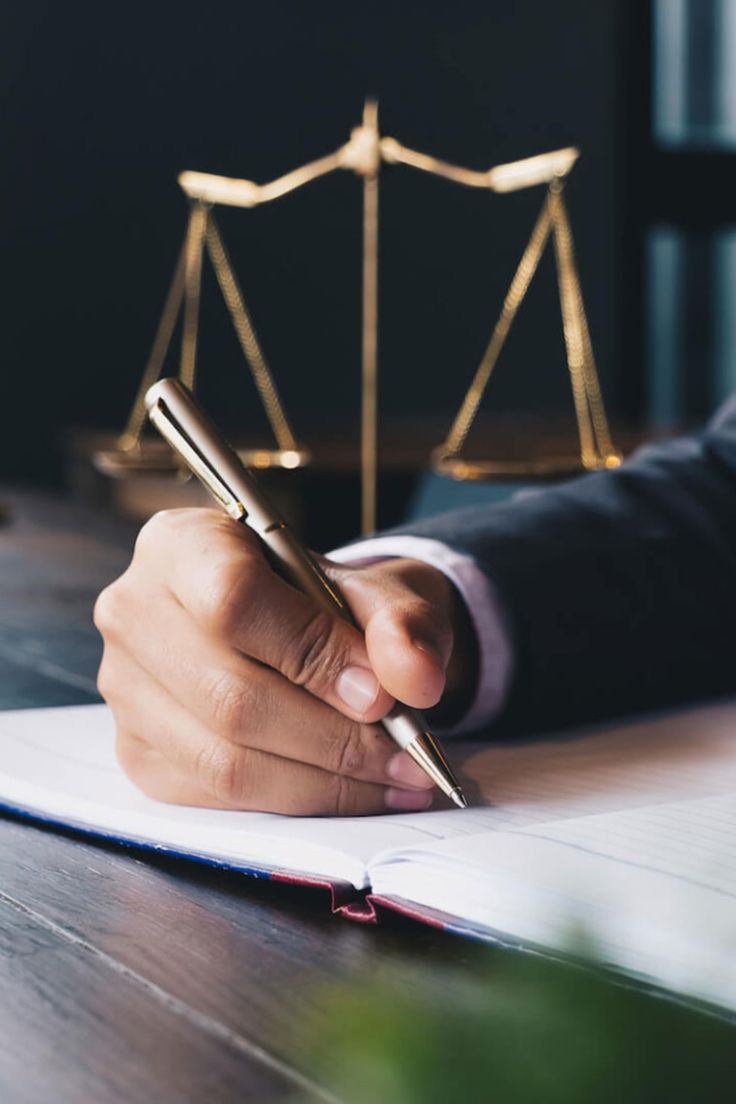 a person holding a pen and writing on a paper with a scale of justice in the background