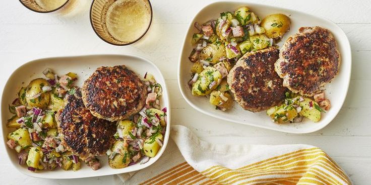 two plates with meat patties and potatoes on them next to an avocado