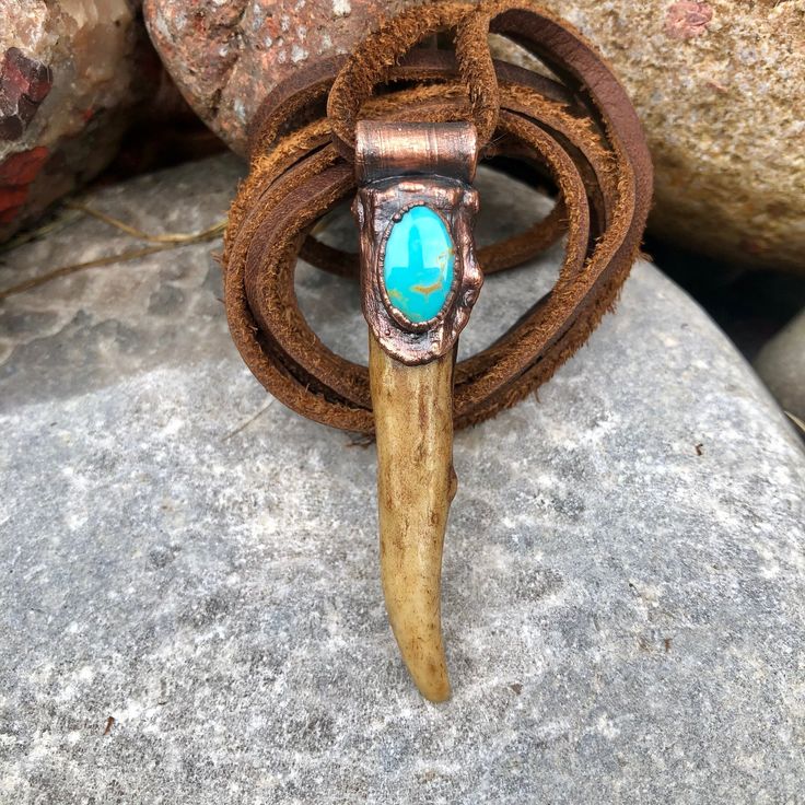 a turquoise stone in the center of a brown leather cord with an animal's horn on it