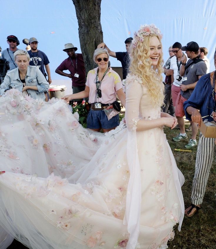 a woman in a white dress with flowers on it and people standing around looking at her