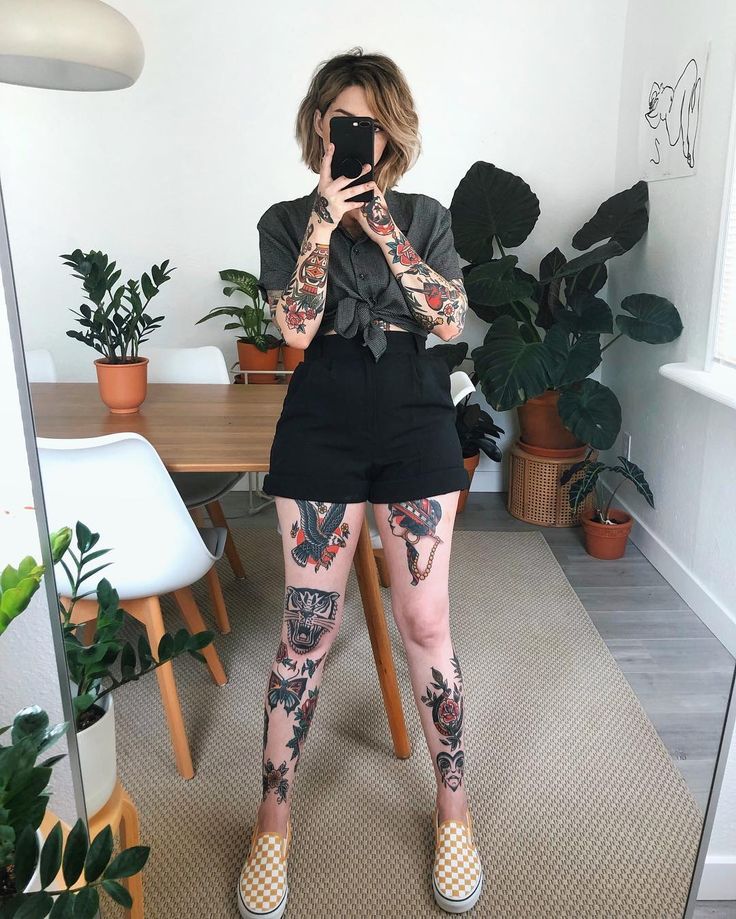 a woman with tattoos taking a selfie in front of a mirror while holding a cell phone