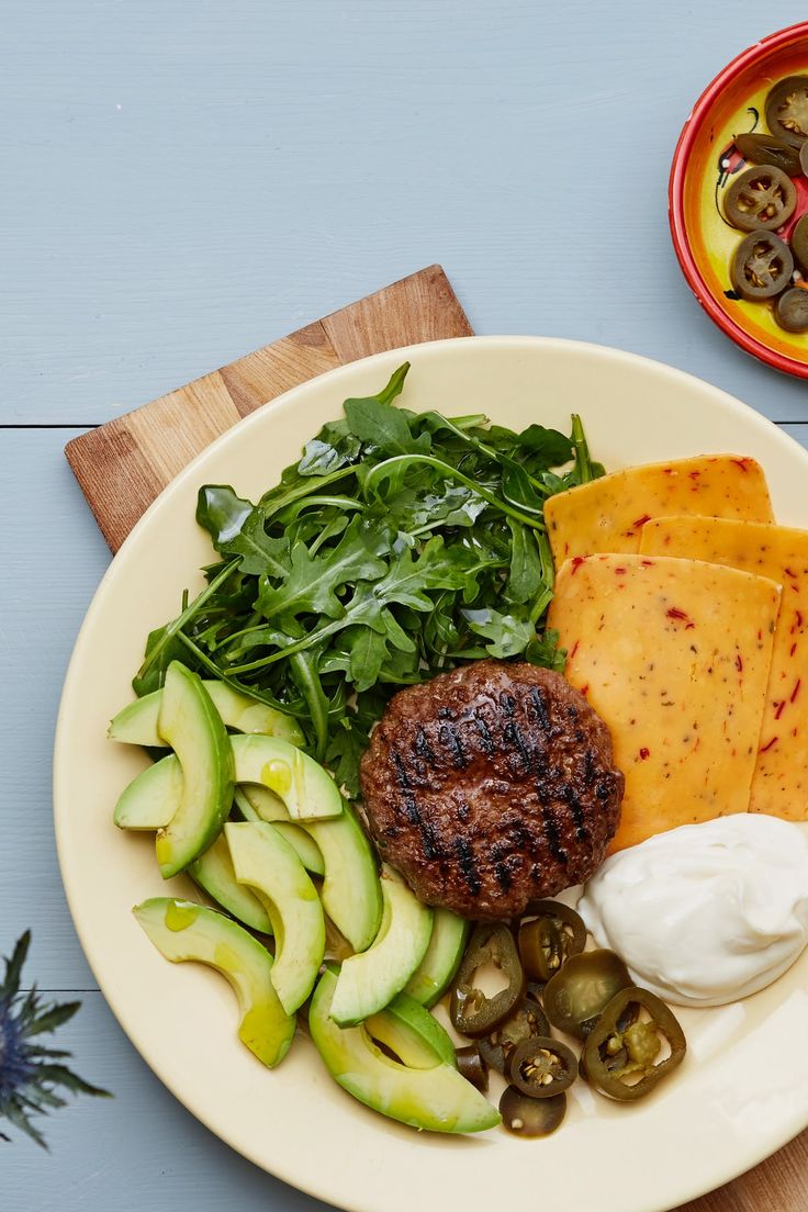 a white plate topped with meat, cheese and veggies next to a bowl of sauce