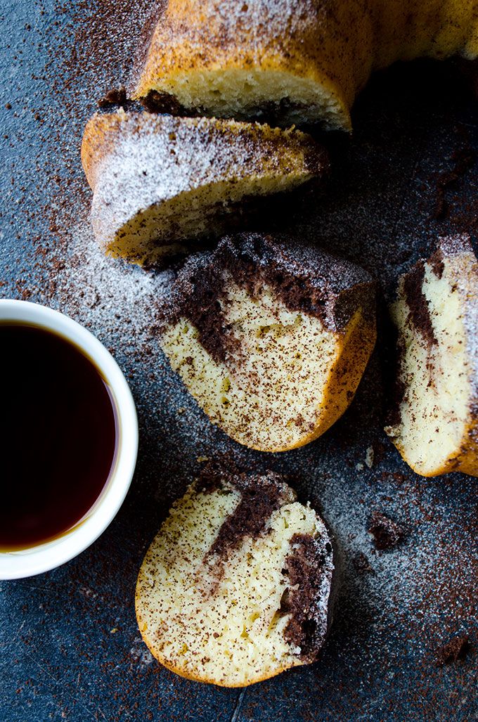 a bundt cake with chocolate frosting and powdered sugar next to a cup of coffee