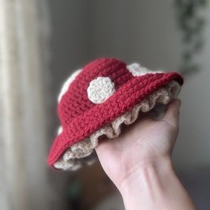 a hand holding a red and white crocheted hat