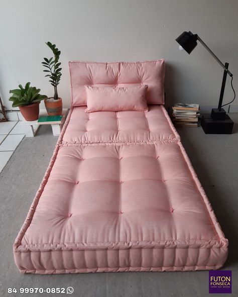 a pink futon bed sitting on top of a floor next to a potted plant