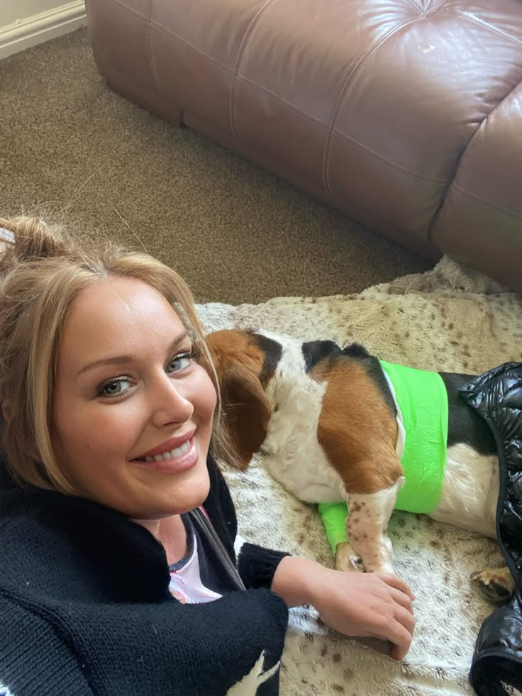 a woman laying on the floor next to a dog wearing a green shirt and boots