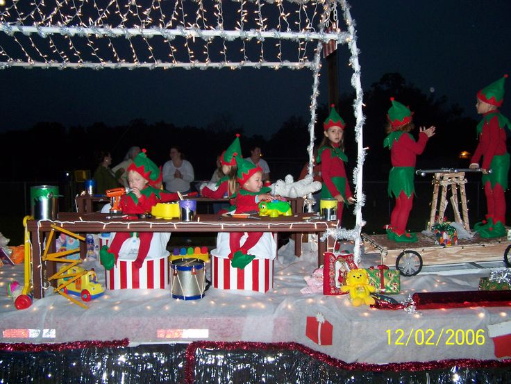 people dressed in elf costumes sitting at a table with presents on it and lights strung from the ceiling