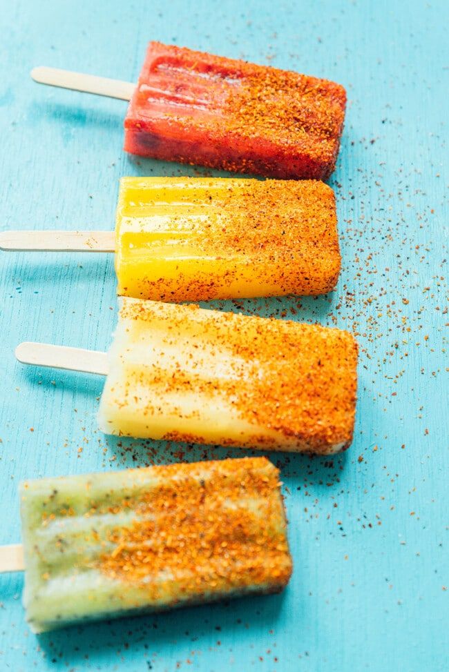 three popsicles are lined up on a blue surface with sprinkles and seasoning