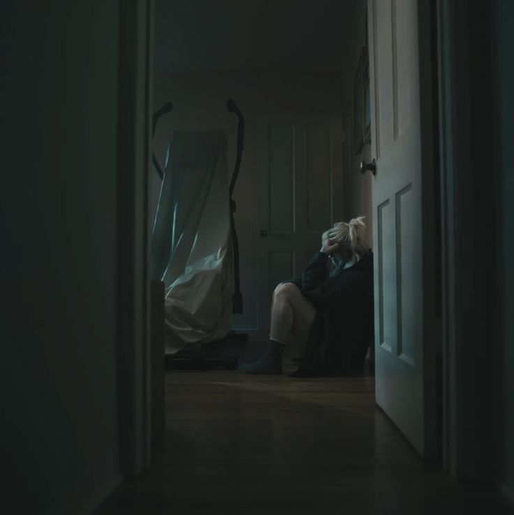 an older woman sitting on a chair in a dark room with her back turned to the camera