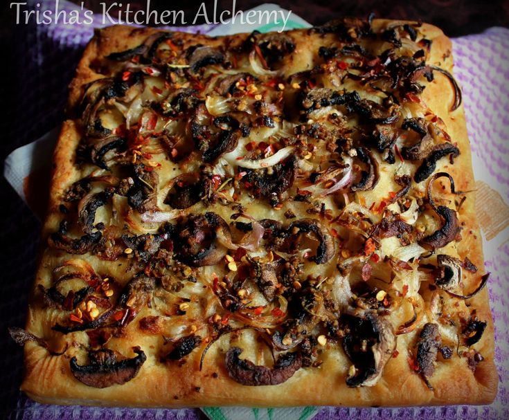 a square pizza with mushrooms and onions on it sitting on a purple cloth covered table