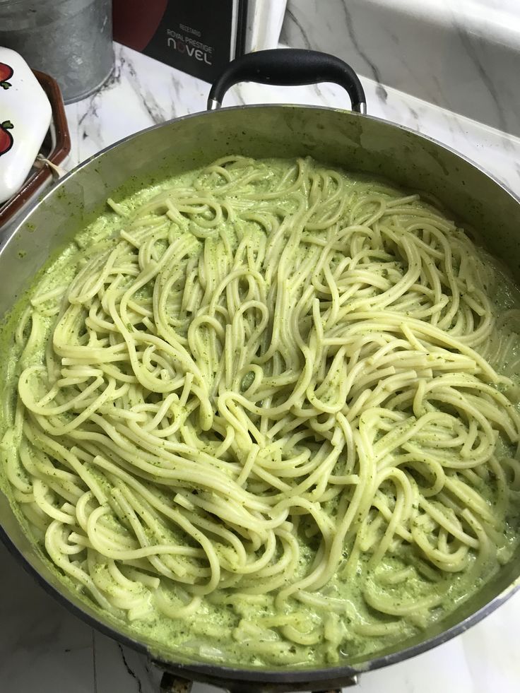 a pan filled with green pasta sitting on top of a stove