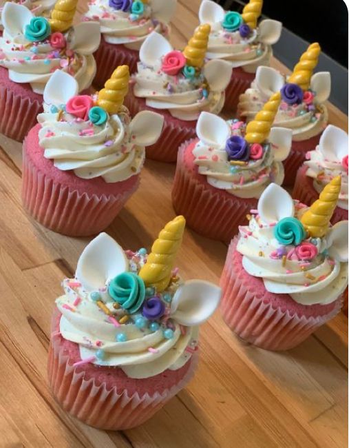 cupcakes decorated with unicorn ears and flowers on a wooden counter top, ready to be eaten