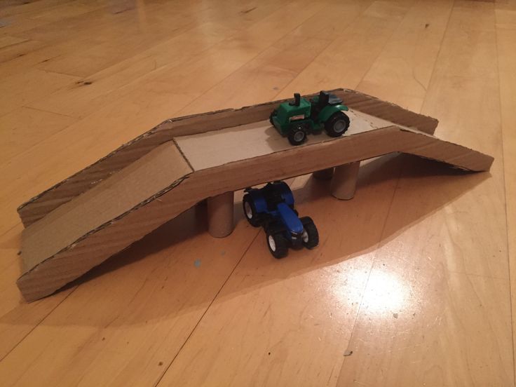 a cardboard box with two toy tractors in it on the floor next to a ramp