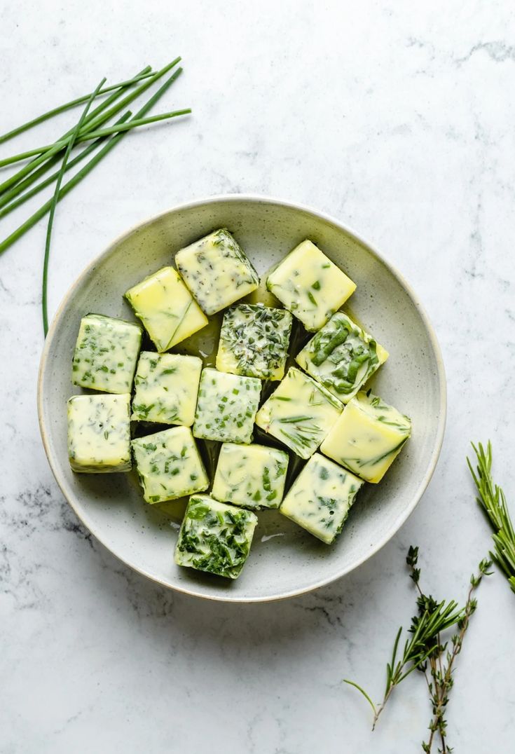 a bowl filled with cheese and herbs on top of a white countertop next to green stems