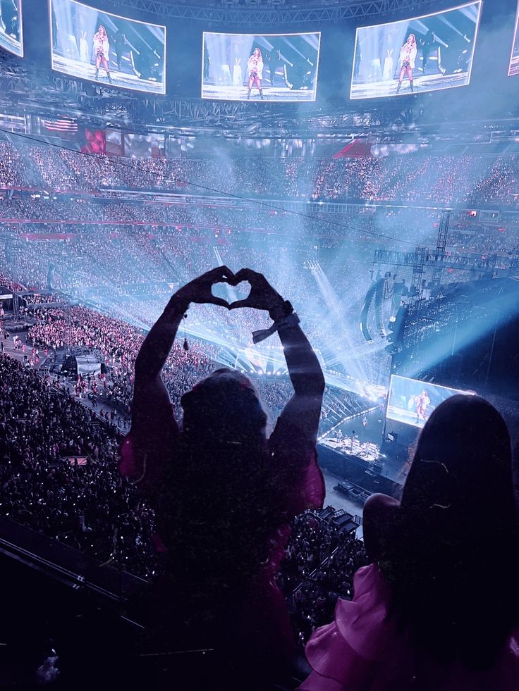 a person holding up a heart in front of a crowd at a concert with lights on