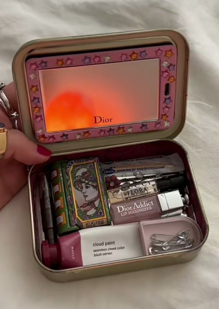 a woman's hand holding an open tin box with various items in it on a bed