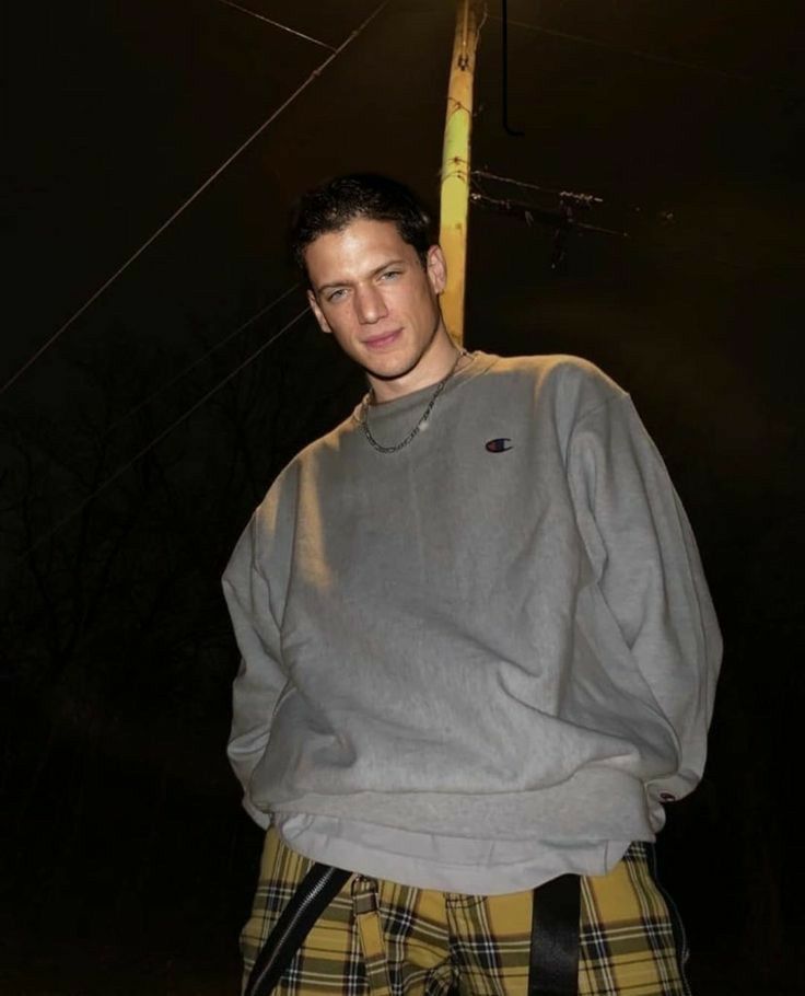 a young man standing in front of a street light wearing a grey sweatshirt and plaid shorts