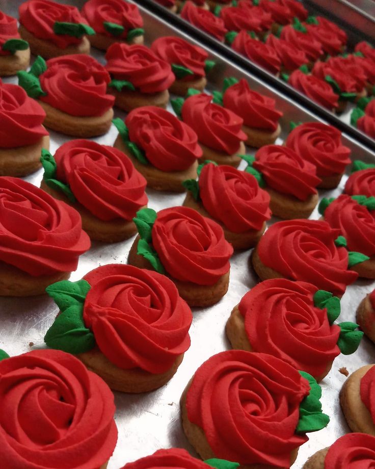 red frosted cupcakes with green leaves and roses are on a baking sheet