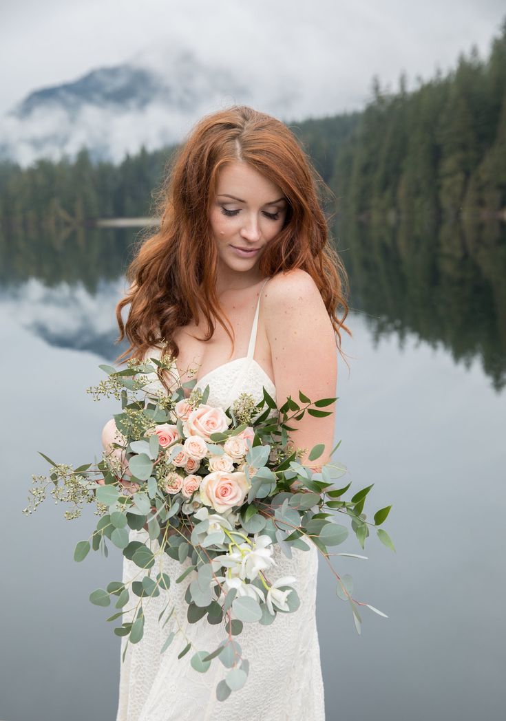 a woman holding a bouquet of flowers in front of a body of water