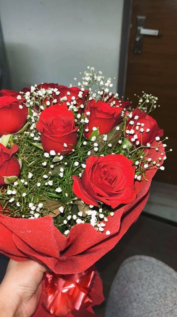 someone holding a bouquet of red roses with baby's breath in the middle,