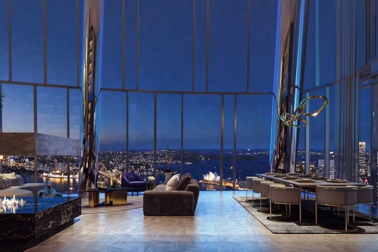 a living room filled with furniture and large windows overlooking the city at night, in front of tall buildings