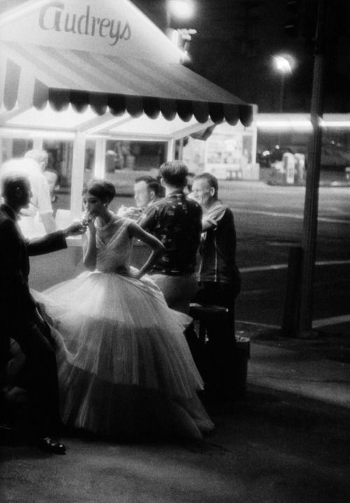 a black and white photo of people in front of a building at night with their luggage