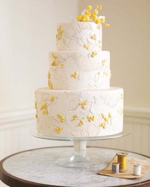 a three tiered white cake with yellow flowers on the top is sitting on a table