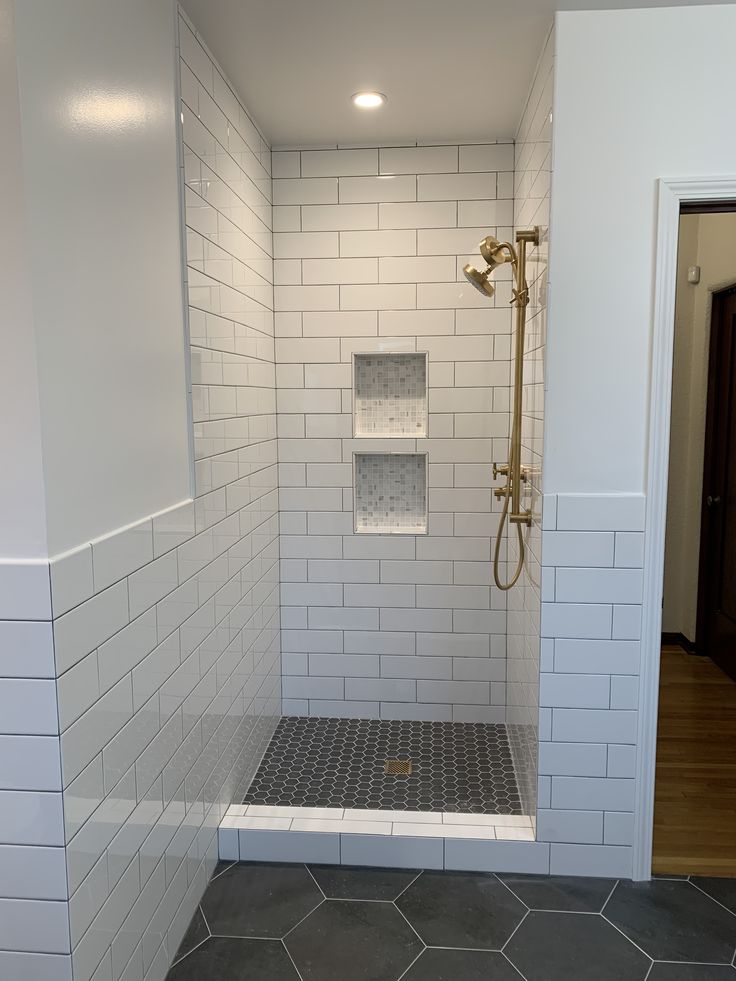 a walk in shower sitting next to a white tiled wall and floor covered in gray tile