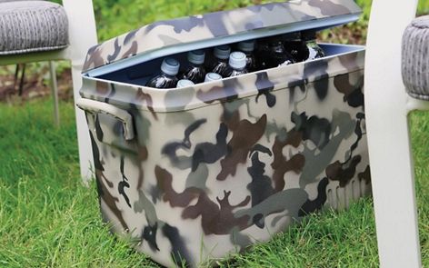 a camo cooler sitting in the grass next to two white chairs with grey cushions